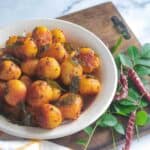 Potato Roast served in a white bowl with curry leaves and red chilies