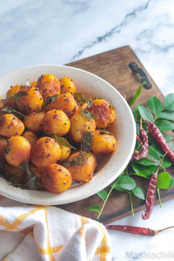Potato Roast served in a white bowl with curry leaves and red chilies