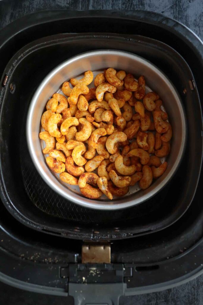 spiced cashew nuts placed in round baking tin inside the air fryer basket