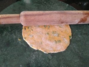 Rolling the rotis by dusting flour and pressing with the rolling pin