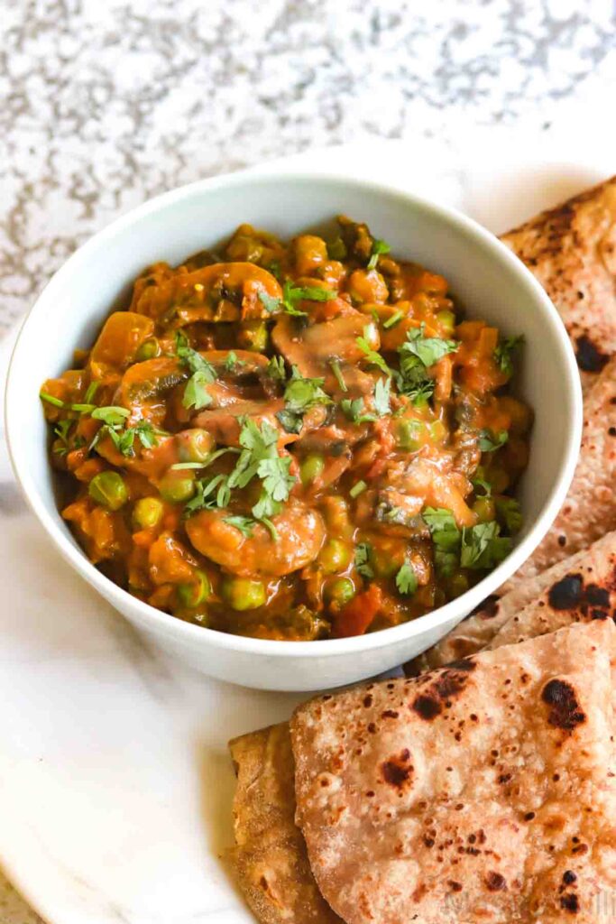Vegan Mushroom Peas curry served in a white bowl with chapati