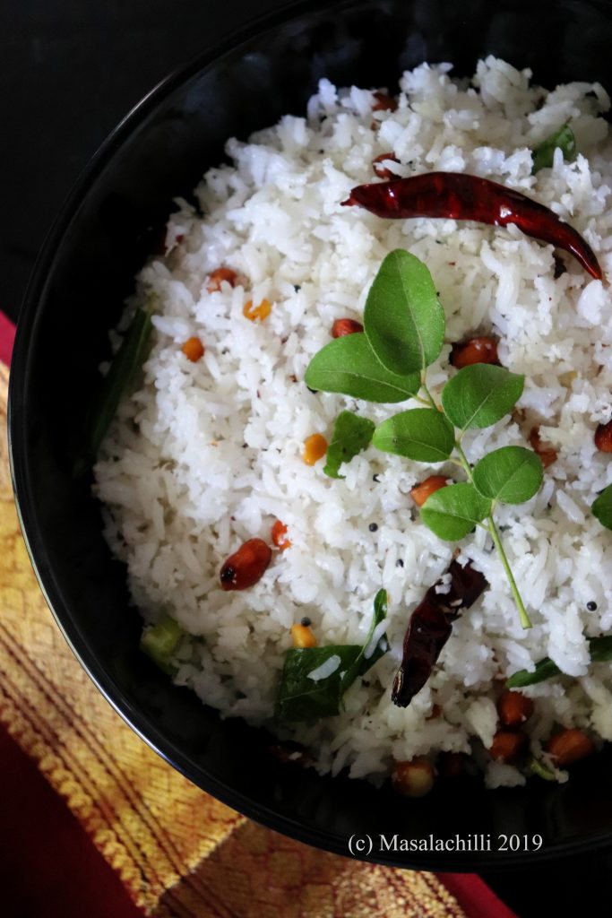Coconut Rice served in a black bowl garnished with peanuts, chana dal, red chili and curry leaf sprig on top