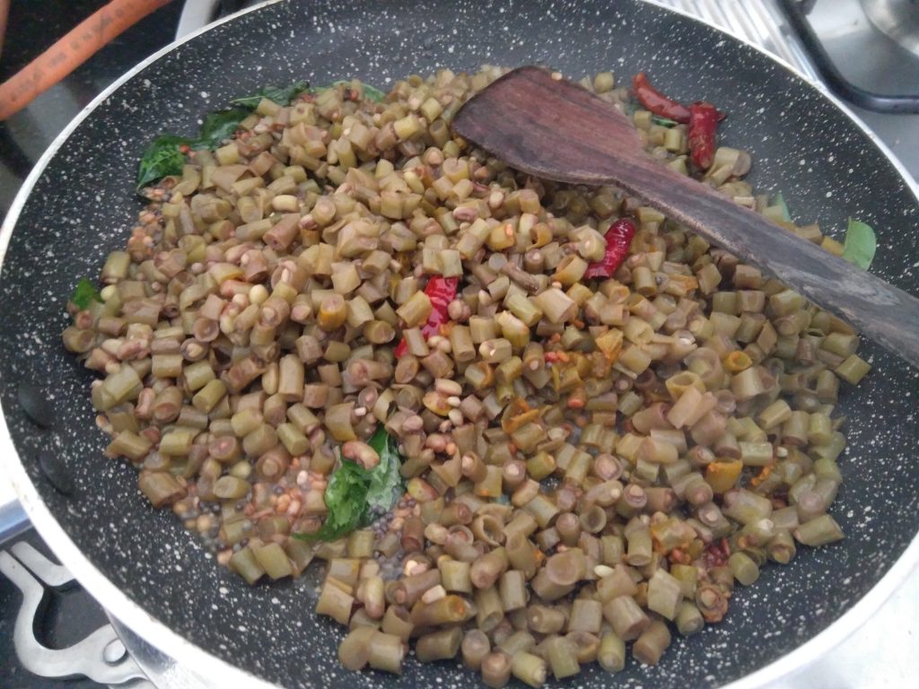 cooked long beans added to mustard seeds and coconut oil