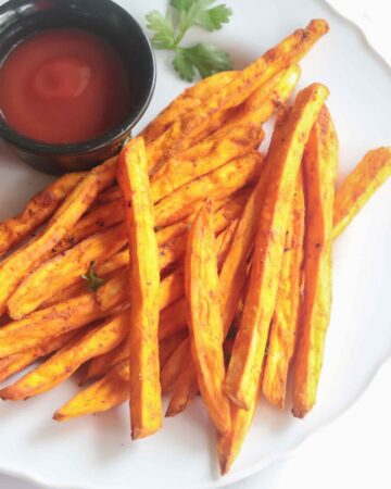 crispy sweet potato fries served with tomato ketchup in a white plate