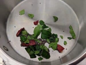 Preparing the tempering with coconut oil, mustard, curry leaves, red chillies and hing