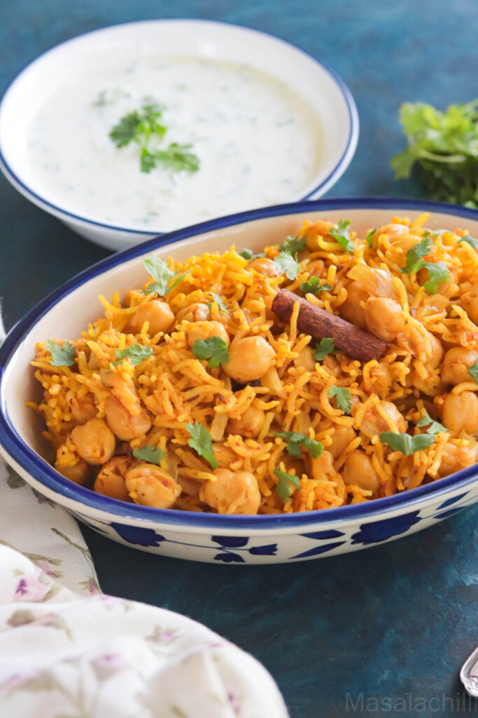 Chickpeas and rice served in a blue rimmed bowl with a side of raita