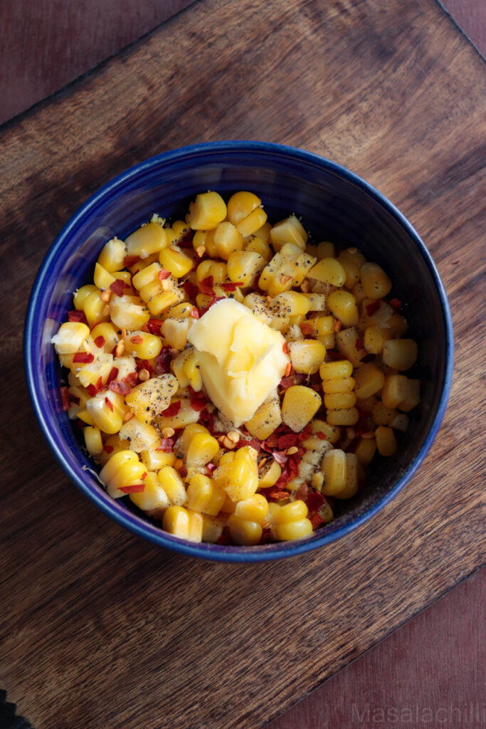 steamed corn in a blue bowl served with butter, chilli flakes, salt and pepper