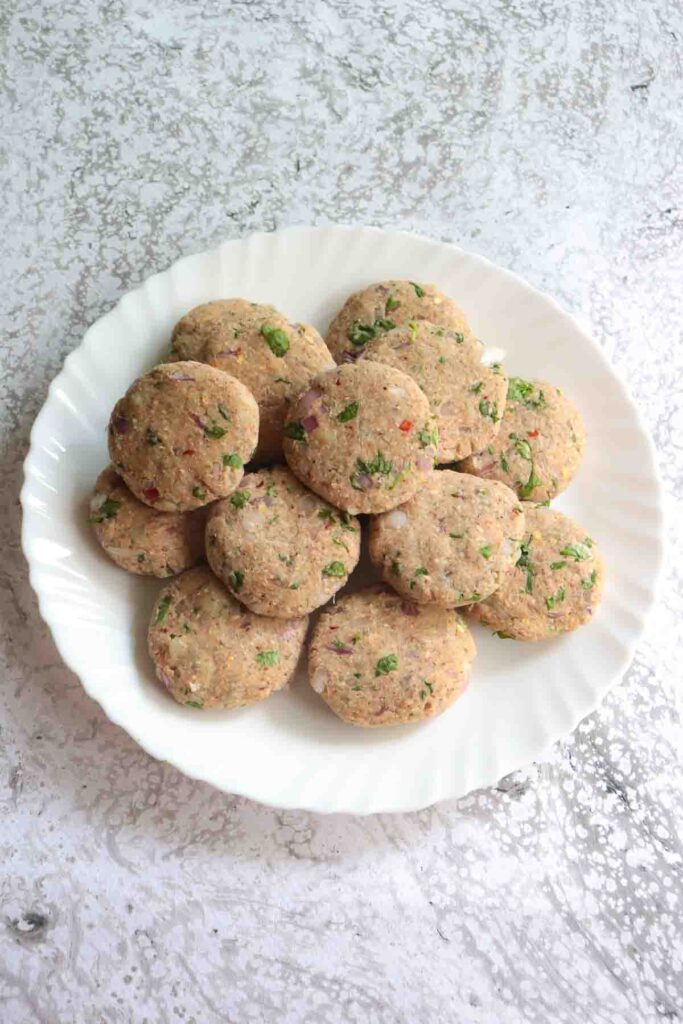 14 quinoa patties on a white plate ready to be refrigerated and baked later