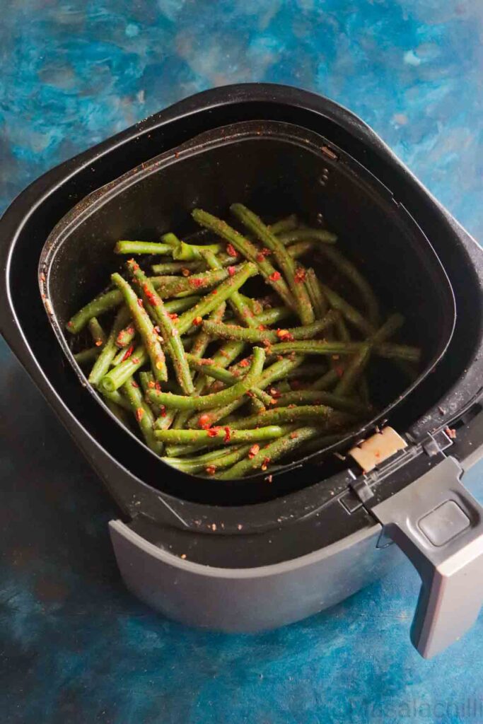 seasoned green beans placed in air fryer basket