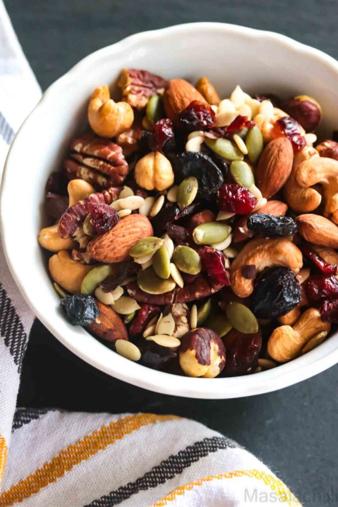 Close up view of trail mix with nuts, seeds and dried fruit in white bowl