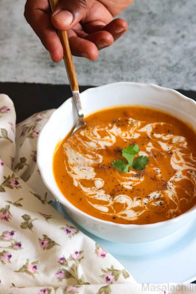 Dunking a spoon into a bowl of tomato bisque