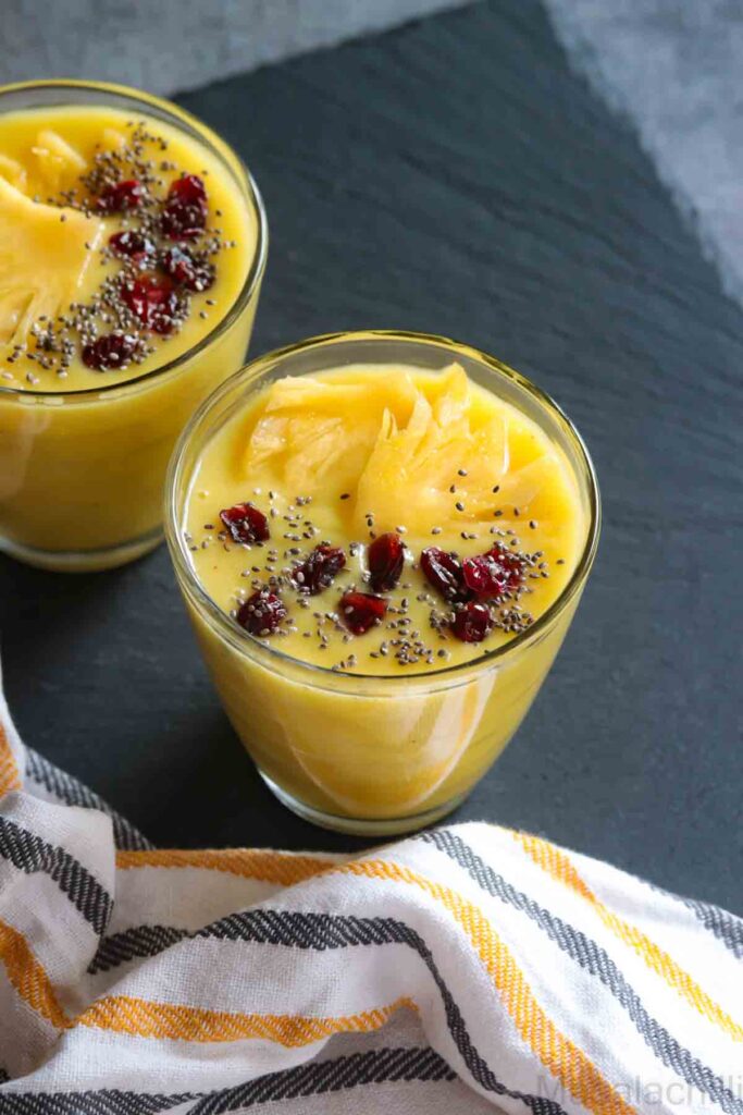 Glass with pina colada smoothie topped with chia, cranberries and pineapple slice