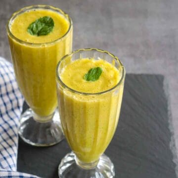 Two Glasses of pineapple ginger smoothie garnished with mint leaf
