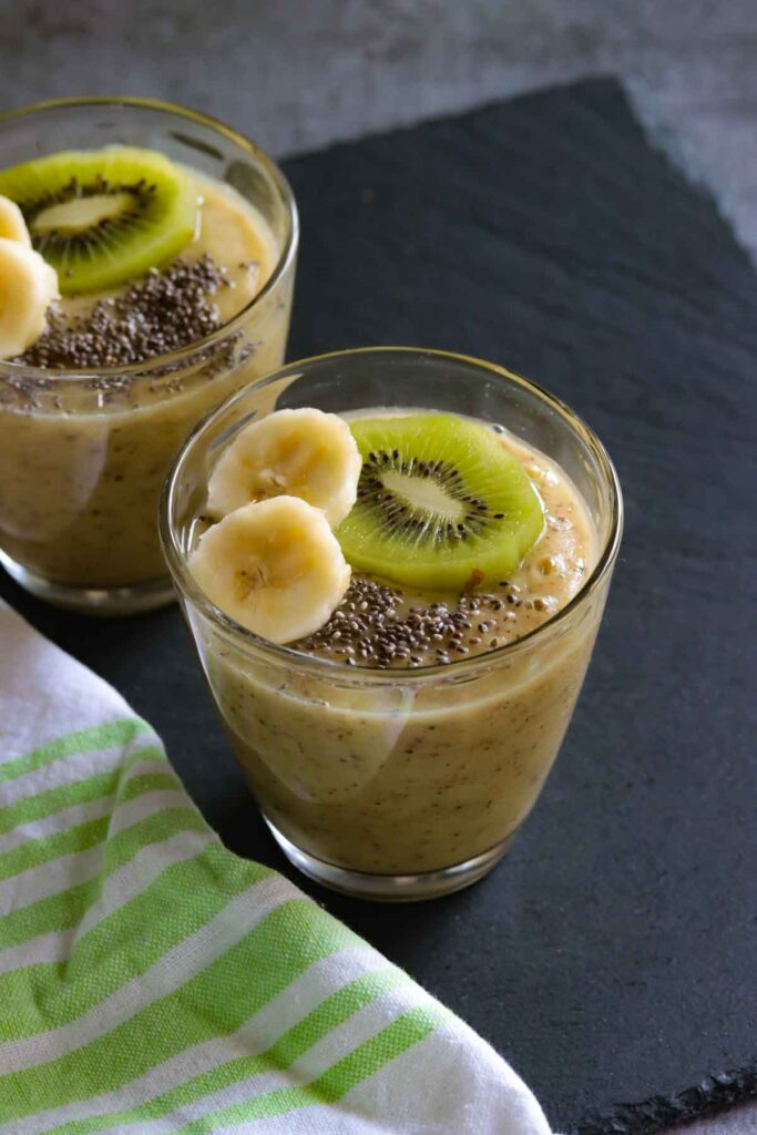 Two Glasses of Kiwi Banana Smoothie topped with banana slices, kiwi slice and chia seeds