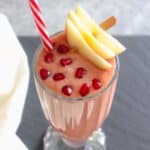 Glass of Pomegranate smoothie topped with pomegranate arils and apple slices with a red straw