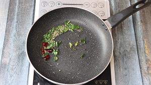 Tempering of mustard seeds, urad dal, curry leaves and red chillies in coconut oil for vendakkai thayir pachadi