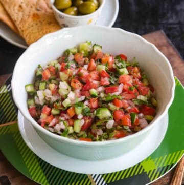 Shirazi Salad served in a white bowl on a green plate with green olives in the background