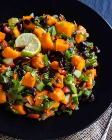 Vegan Black Bean Mango Salad served in a black bowl with lime wedges