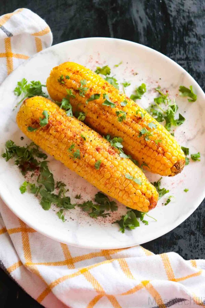 Corn on the Cobs served on a white plate and garnished with cilantro, paprika and black pepper