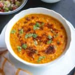 Moong dal topped with tempering and coriander leaves served in a white bowl with a bowl of basmati rice and kachumber salad on the side