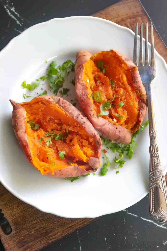 2 Baked Orange sweet potato served on a white plate garnished with cilantro, black pepper, red chili flakes and salt