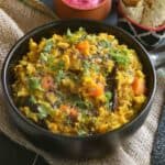 Dal khichdi with vegetables served in a black bowl with papad and raita