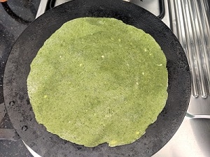 cooking spinach paratha on a hot iron griddle