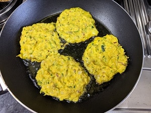 cooking zucchini fritters on a griddle with extra virgin olive oil