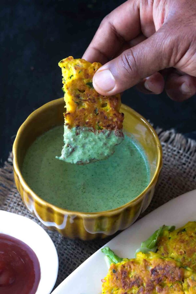 a piece of zucchini fritters dipped in yogurt mint sauce